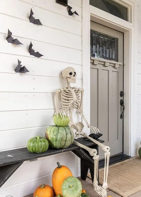 Eskitilmiş balkabakları, iskelet ve duvardaki yarasalarla rustik tarzda bir Halloween verandası.