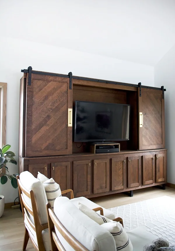 Koyu renkli, vintage tarzda ve sürgülü kapaklı şık bir dolap; TV'yi gizlerken şıklığını ortaya koyuyor.
