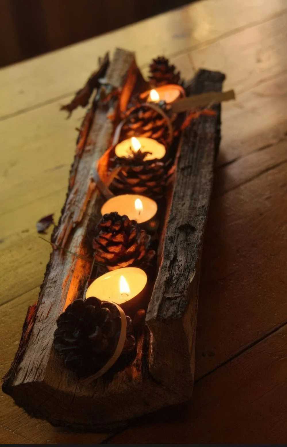 Çam kozalakları ve tealight mumlarla süslenmiş ağaç kütüğü, sonbaharı yansıtan rustik ve havalı bir masa ortasıdır.