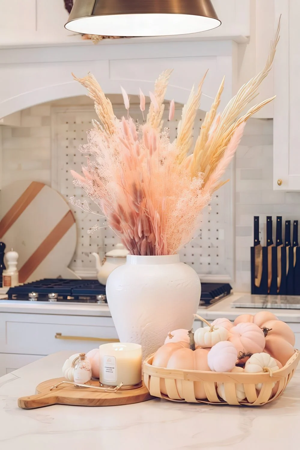 Pastel tonlarda bir ahşap tepsi içinde balkabakları, mum ve vazoda kurutulmuş bitkilerle sonbahar ortası.