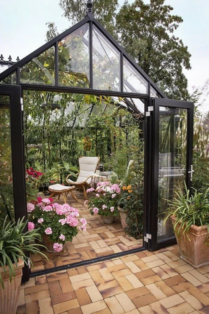 Küçük cam sera, yeşillik ve çiçeklerle güzel bir orangery, ayak destekli rahat bir sandalye ile manzaranın keyfi.