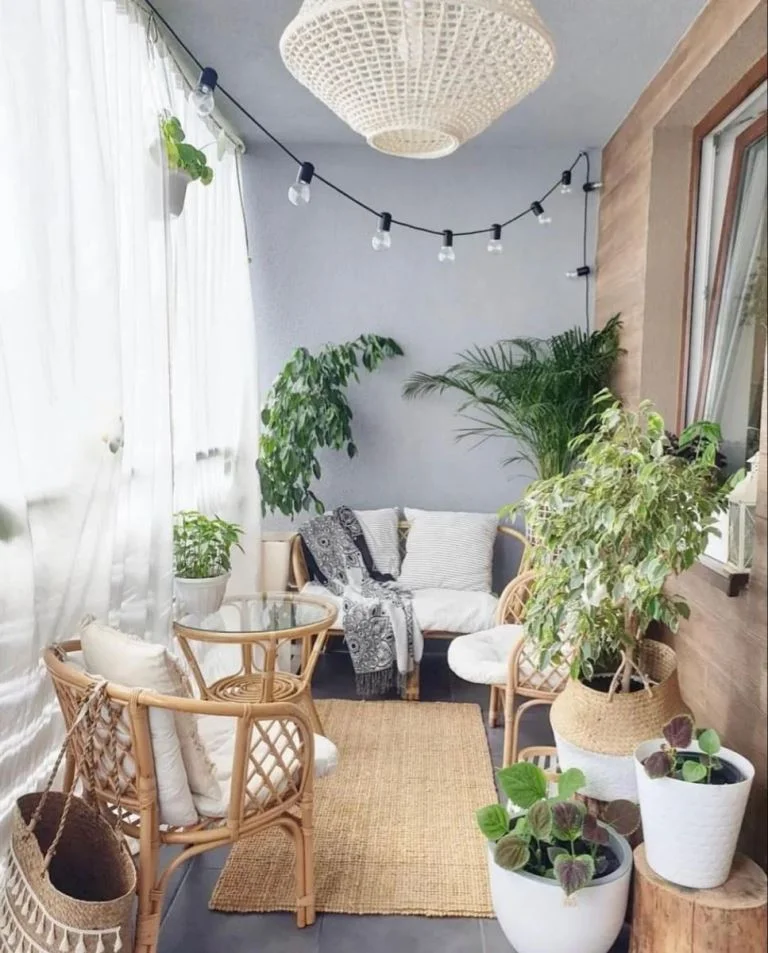 Gri duvarlar, rattan mobilyalar, saksı bitkiler ve ince tüllerle balkon tam bir dış mekan oturma alanı olarak düzenlenmiş.
