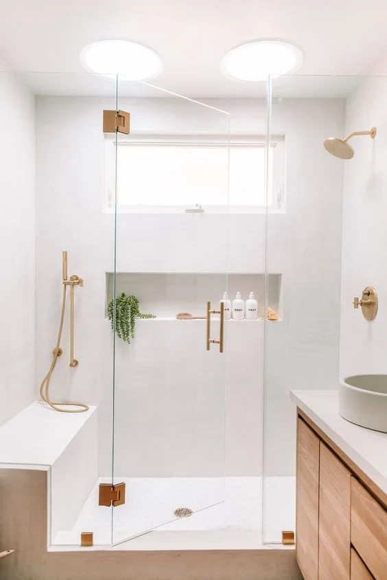 Beyaz duvarlar, lekeli lavabo, bank ve duşta niş, altın detaylar ile hoş nötr banyo.