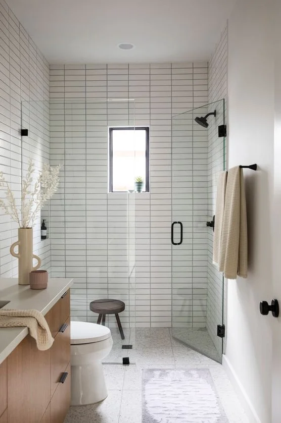 Beyaz ince fayanslarla kaplı, şık lavabo, siyah armatürler ve duşta küçük pencereye sahip huzurlu küçük banyo.