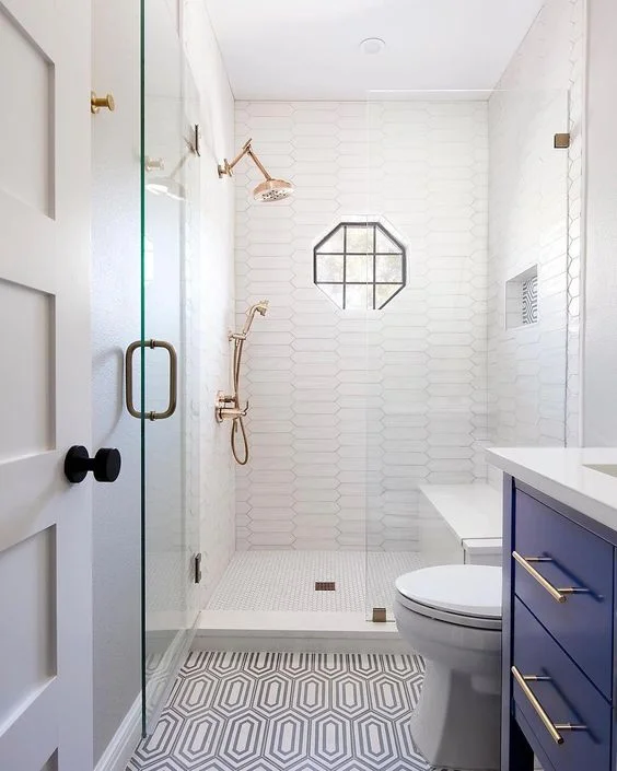 Uzun göz alıcı fayanslı duş, desenli zemin, cesur mavi lavabo, pirinç detaylar ve geometrik pencereli şık küçük banyo.