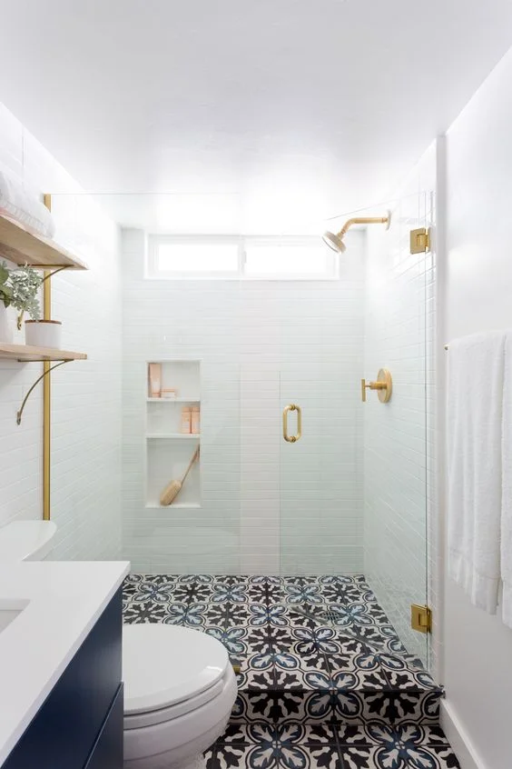 Beyaz duş karoları, desenli zemin, lacivert bir lavabo ve altın dokunuşlarıyla küçük modern banyo.