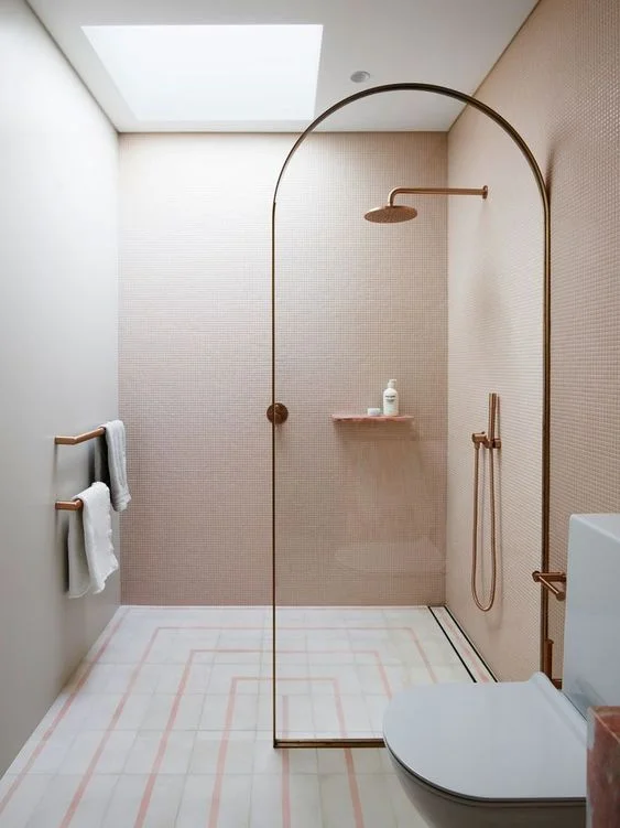 Pembe duvarlar, desenli zemin, cam bölme ve gül altını detaylarıyla küçük minimalist banyo.