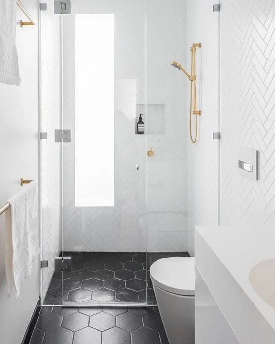 Beyaz kılçık ve siyah altıgen fayanslı küçük banyo. Sırttan buzlu pencere ve altın armatürler mevcut.