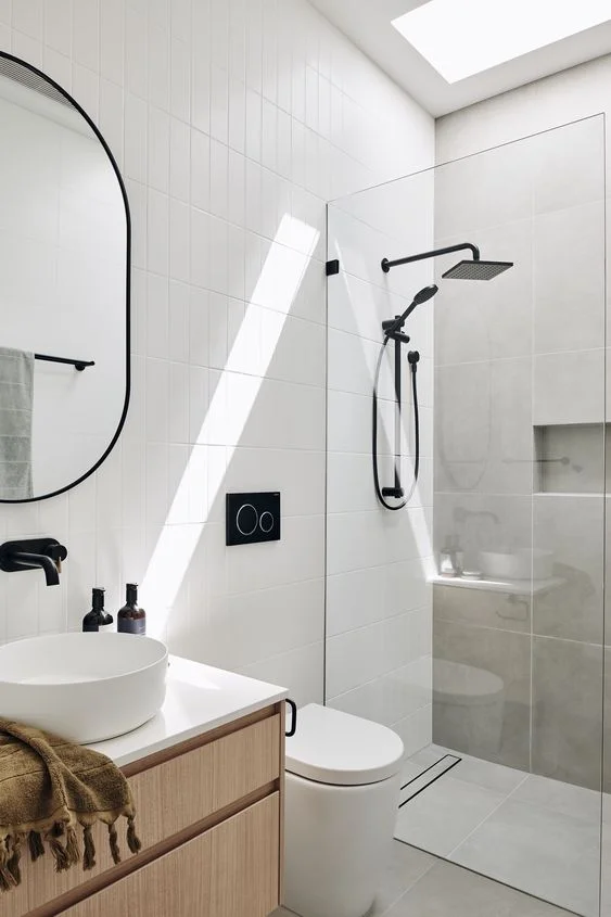 Gri beton ve beyaz ince karolarla kaplı, renklendirilmiş lavabo ve siyah armatürlü çağdaş küçük banyo.