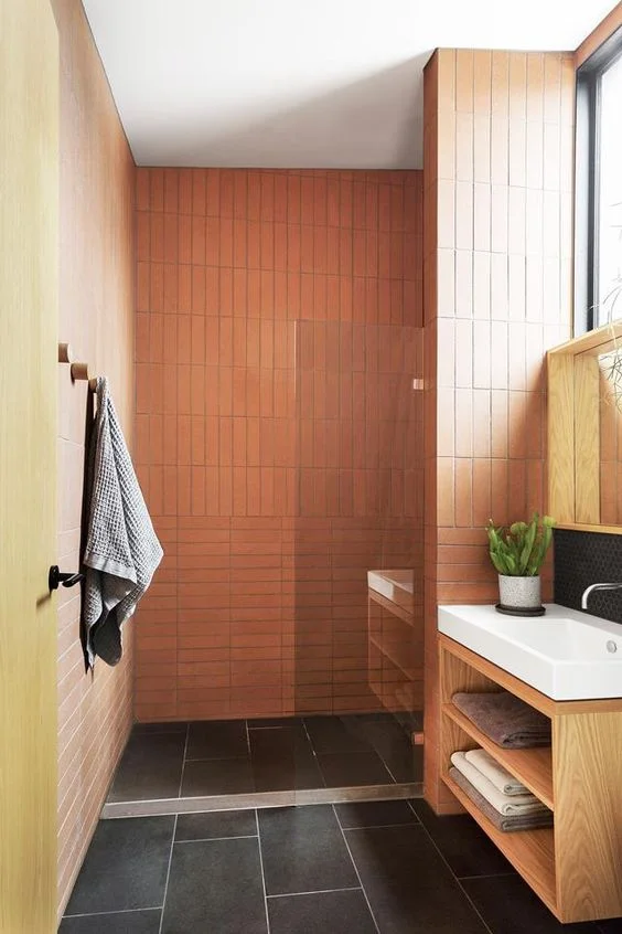 Turuncu ve sarı duvarlar, siyah zemin karoları, lekeli lavabo ve beyaz cihazlar ile aydınlık banyo.