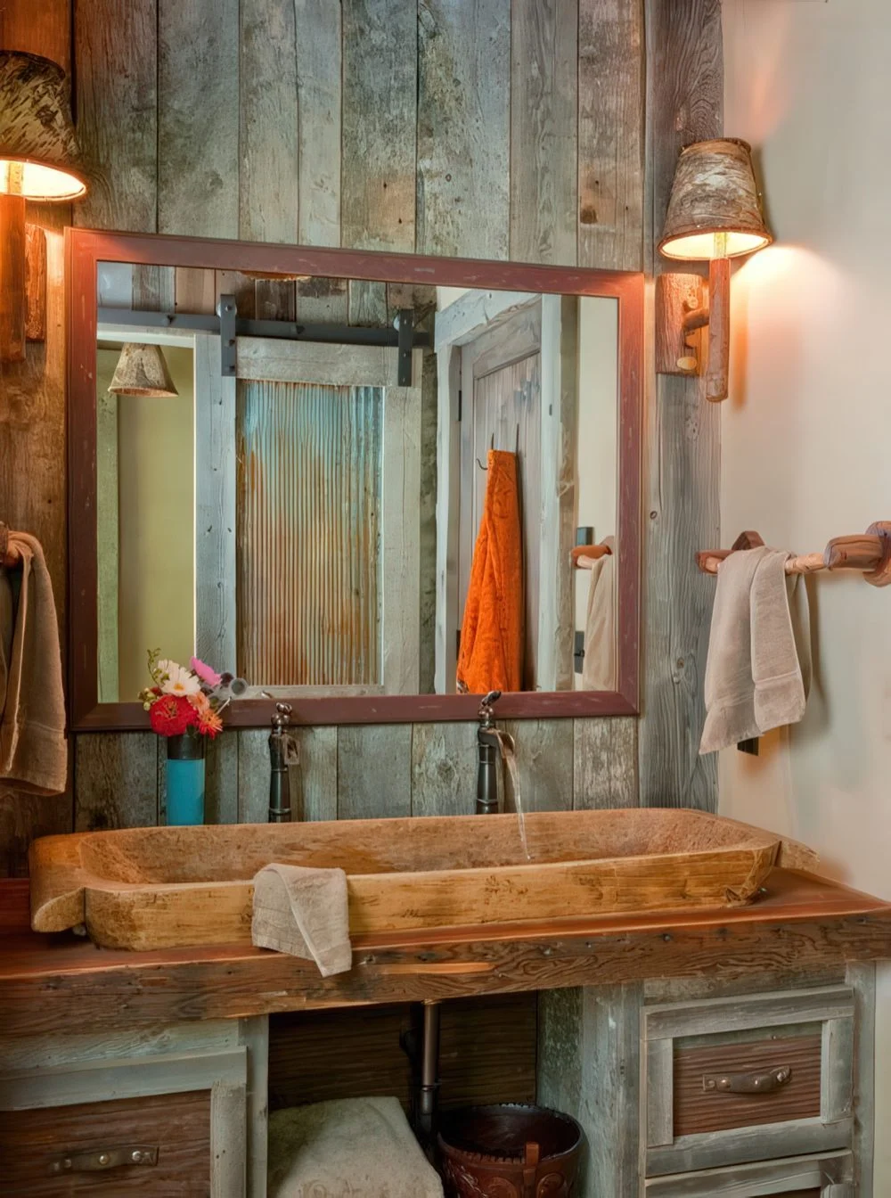 Geri dönüştürülmüş ahşap kaplama, çerçeveli büyük ayna ve taş lavabolu geniş bir banyo dolabı olan ahır banyosu.