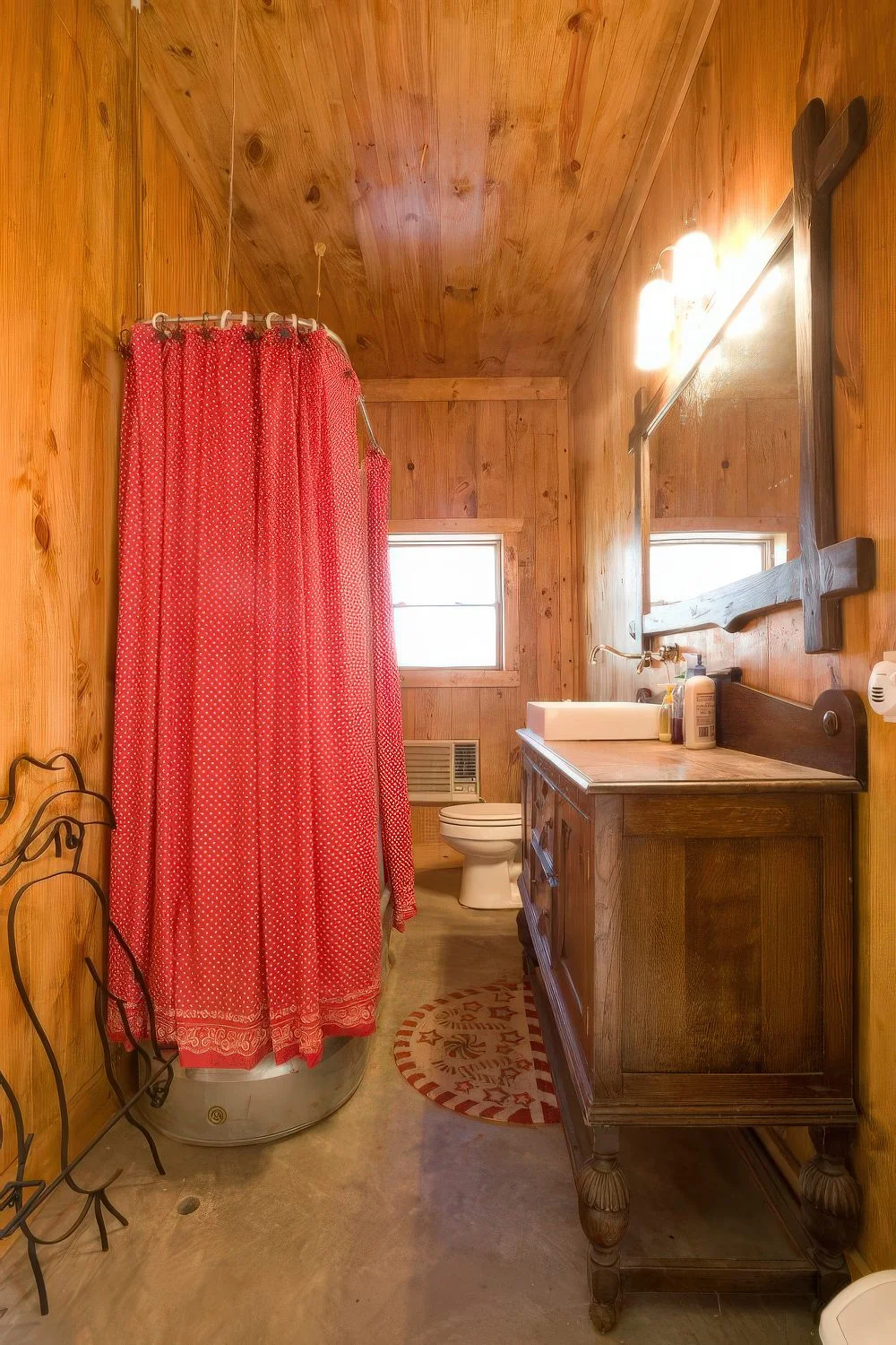 Ahşap kaplamalı sıcak bir ahır banyosu, ahşap lavabo dolabı, büyük ayna, metal küvet ve parlak kırmızı perde.