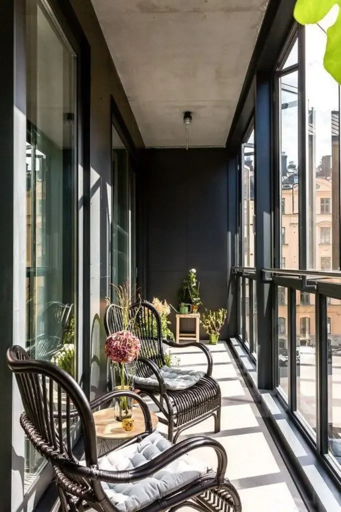 Balkon modern tarzda, siyah bir dolap ve pencere çerçeveleriyle uyumlu koyu renkli rattan sandalyelerle döşenmiş.