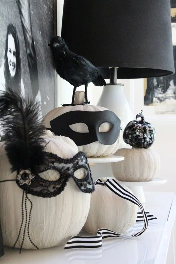 Siyah süslemeli maskeler ve tüylerle şık beyaz kabaklar, Halloween için kolayca yapılabilen harika bir dekor.