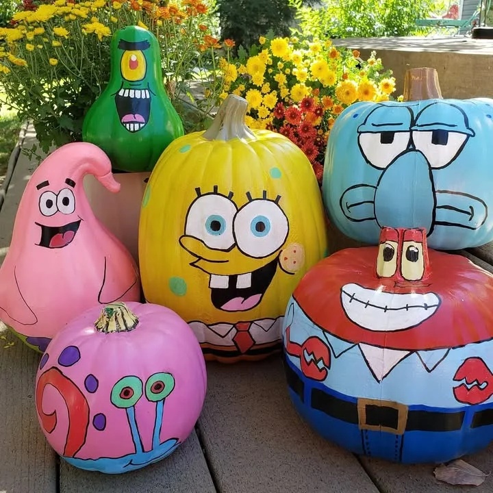 SpongeBob karakterleri Patrick, Squidward, Gary ve Mr. Krabs'ın boyalı renkli kabakları, sarı krizantem çiçekleriyle çevrili; aileler ve çocuklar için eğlenceli kabak süsleme fikri.