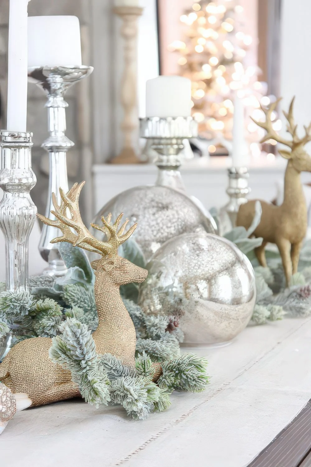 Büyük gümüş süsler, gümüş mumluklar, karla kaplı yeşillikler ve altın renkte geyiklerle nostaljik Noel dekorasyonu.