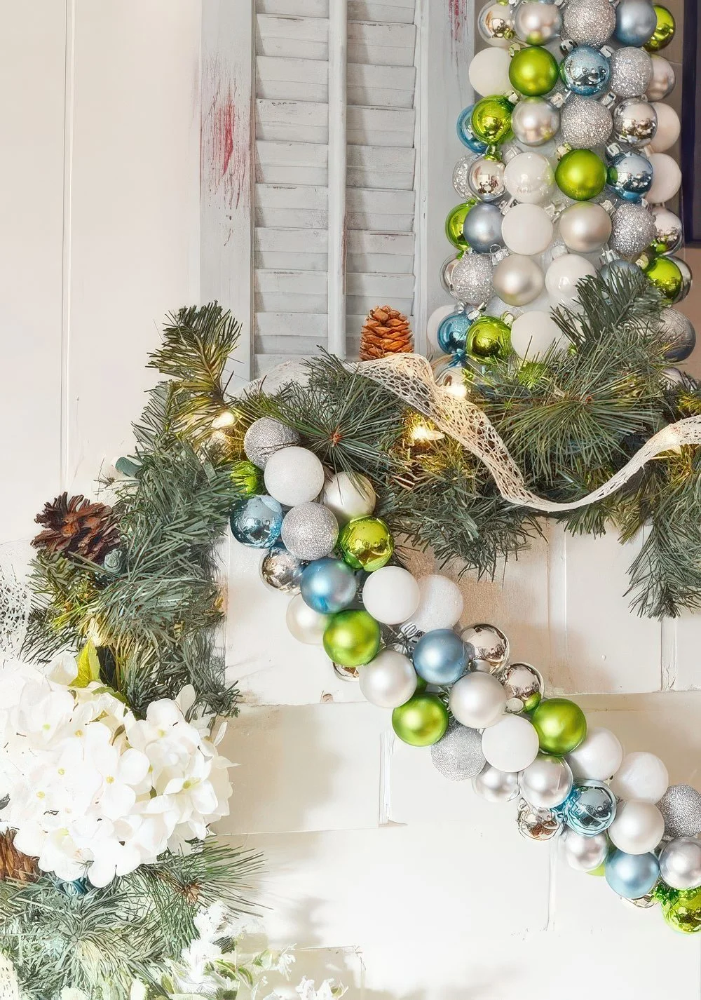 Şömine rafının üzerinde yeşil, beyaz ve mavi Noel süslerinden oluşan şık bir tatil süslemesi.