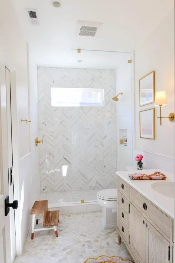 Balık sırtı ve mermer karolar, duş alanı, lekeli lavabo ve altın armatürlü seçkin nötr banyo.