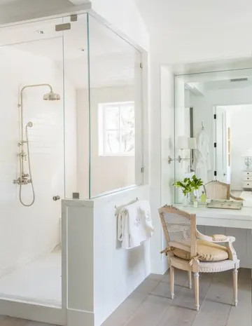 Yarım duvarlı duş alanı, ayna ve vintage sandalyeli nötr antika banyo.