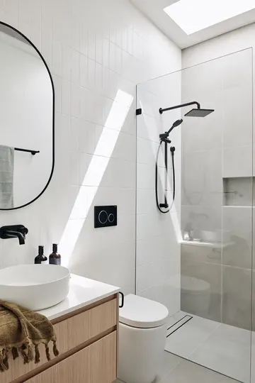 Gri beton ve beyaz ince karolarla kaplı, renklendirilmiş lavabo ve siyah armatürlü çağdaş küçük banyo.