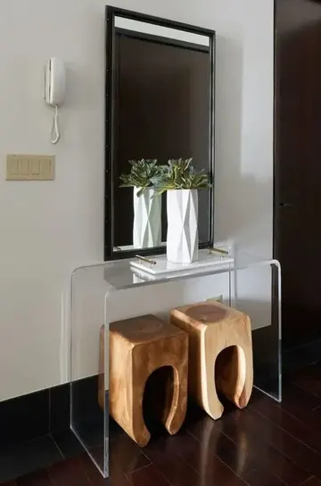 Minimalist akrilik konsol masa, ahşap tabureler, geometrik vazoda yeşillik ve büyük dekoratif ayna.