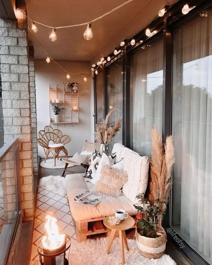 Güzel bohem balkon, sandık koltuk, rattan sandalyeler, mini ateş çukuru ve her yerde asma ışıklarla dekore edilmiş.