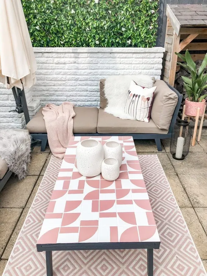 Geometrik fayansla kaplı bu masa mekâna karakter katıyor, geometrik halı ve pembe saksı ile desteklenmiş.