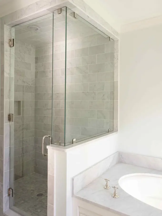 Nötr renkte, küçük fayans kaplı duş alanı, pony divar ve cam bölmeli, gömme lavabo olan banyo.