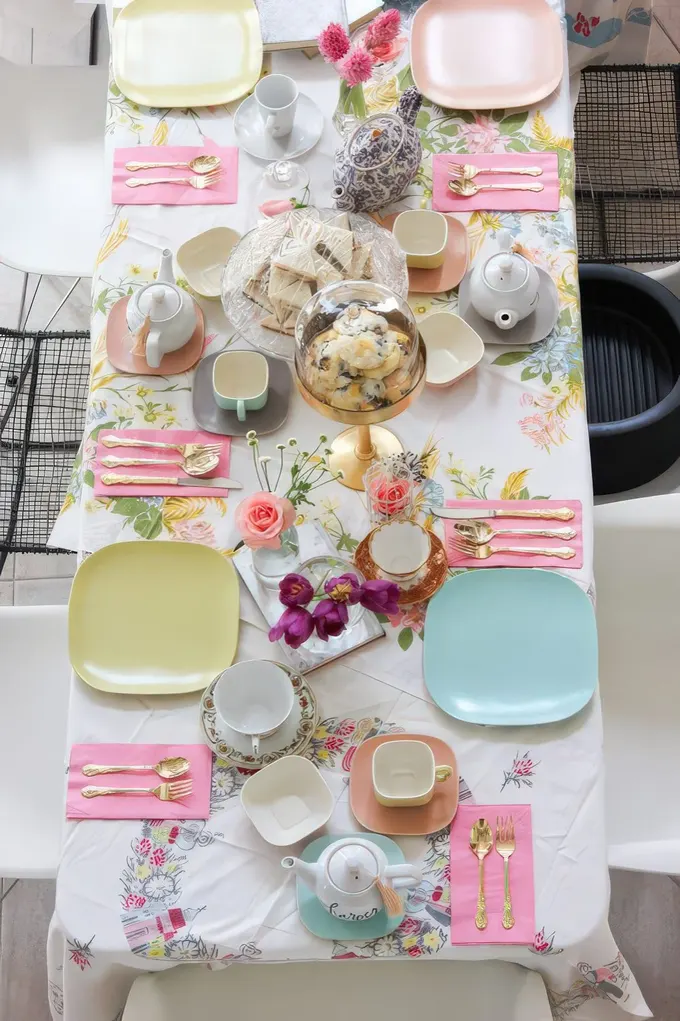Pastel renklerde karışık tabaklar, altın çatal kaşık takımı ve scone ekleriyle tatlı bir çay partisi. Kız bebek partisi için vintage ve şirin bir masa düzeni.