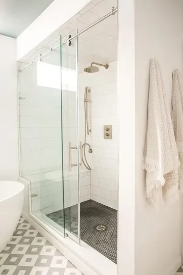Beyaz kare, siyah küçük yuvarlak ve geometrik fayanslı nötr banyo, kayar kapılı duş alanı ve oval küvet.