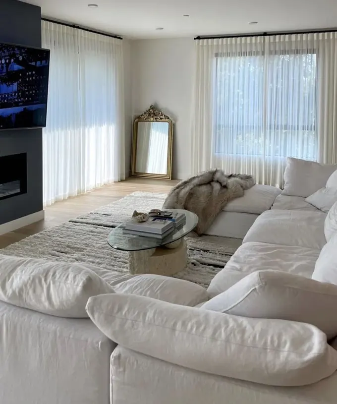 Beyaz slipcover kanepe koyu şömine duvarıyla kontrast oluşturuyor, cam masa ise zarif bir uyum sağlıyor.