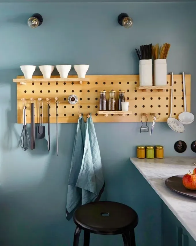 Küçük boyalı pegboard’da mutfak gereçleri, baharatlar ve kaseler var; küçük ama kullanışlı.