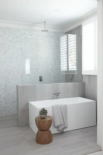 Mermer balık pulu desenli nötr modern bir banyo, yarım duvar nötr ahşap kaplı ve taban aynı malzemeyle döşenmiş.