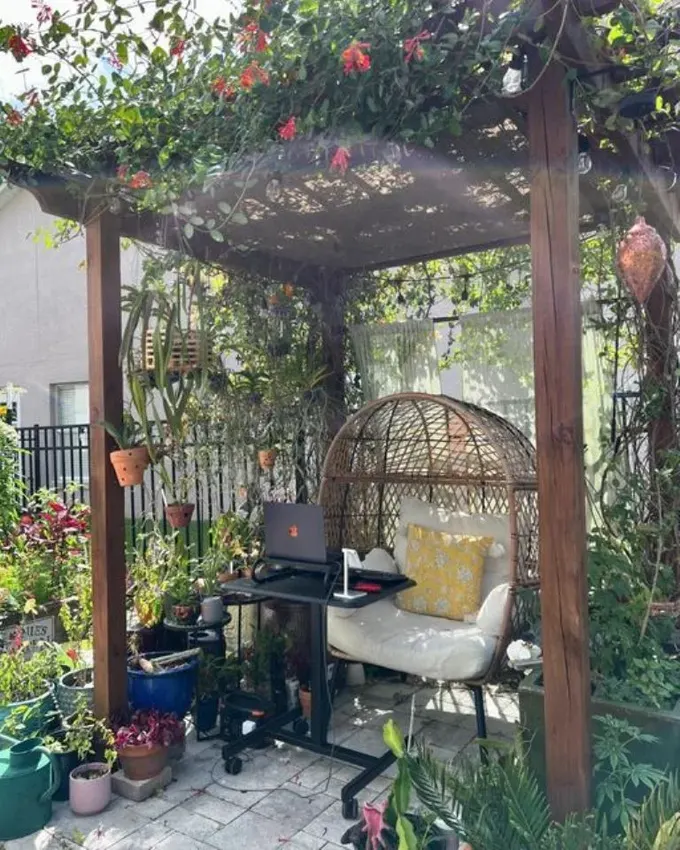 Bir pergola da çalışma alanına dönüşebilir; sepet sandalye, masa ve üstü çiçekli sarmaşıklarla dolu.