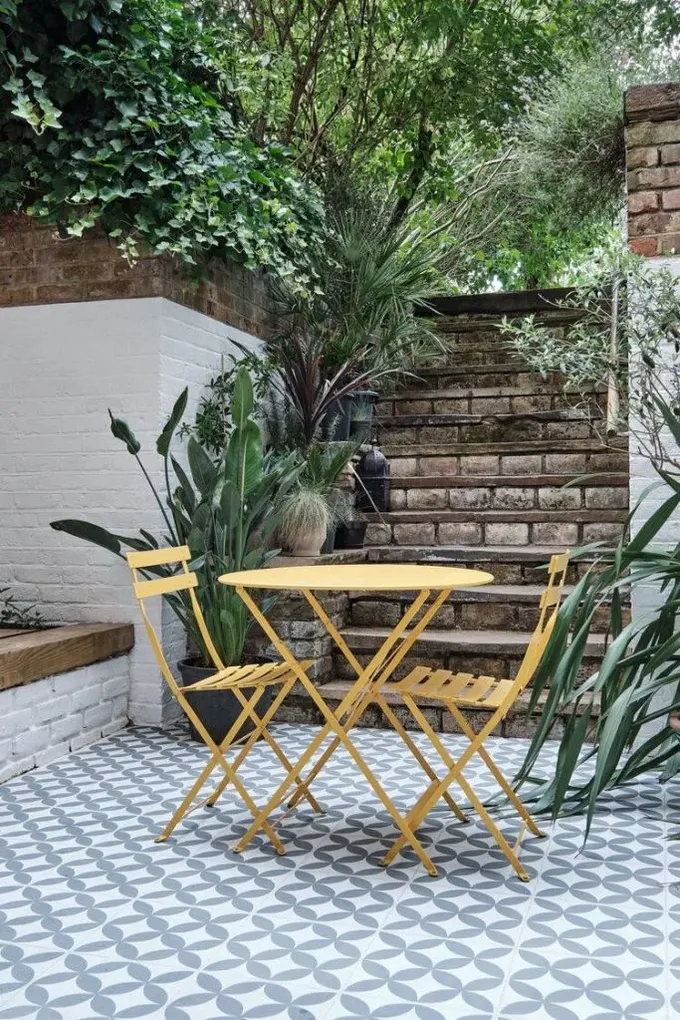 Modern veranda gri ve beyaz çimento karolar, sarı katlanır mobilya ve saksı tropik bitkilerle tamamlanmış.