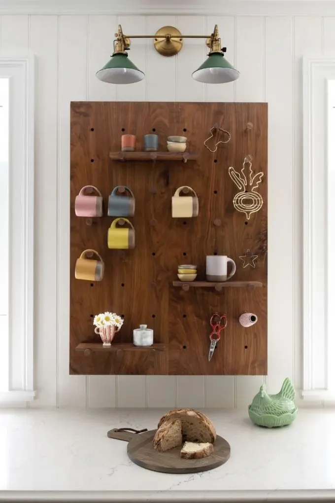 Koyu renkli pegboard, raflar ve kancalarla kupaları saklıyor ve nötr alanla hoş bir kontrast yaratıyor.