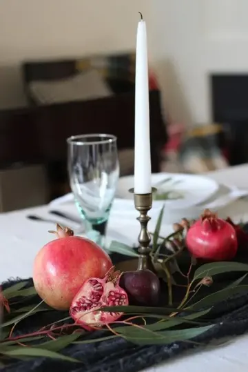 Masa koşucu, yeşillikler, nar, erik ve uzun mumla hazırlanan sade ve güzel bir sonbahar masa ortası.