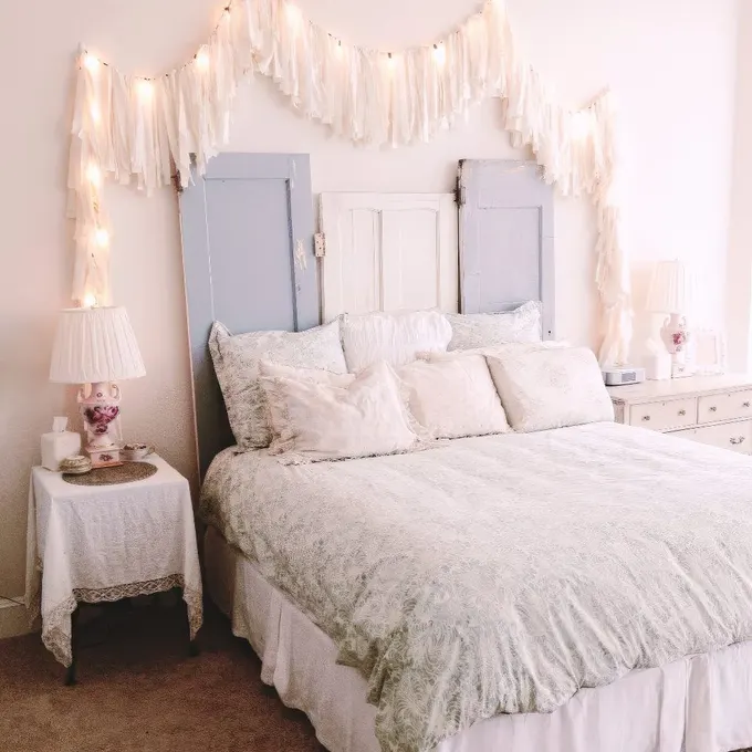 Eski kapılardan yapılan başlık, püsküller ve ışıklarla sıcaklık katan vintage ve shabby chic tarzda nötr yatak odası.