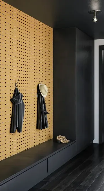 Modern antrede şık siyah dolaplar, depolama bankı ve sarı pegboard duvar askılarla birlikte yer alıyor.
