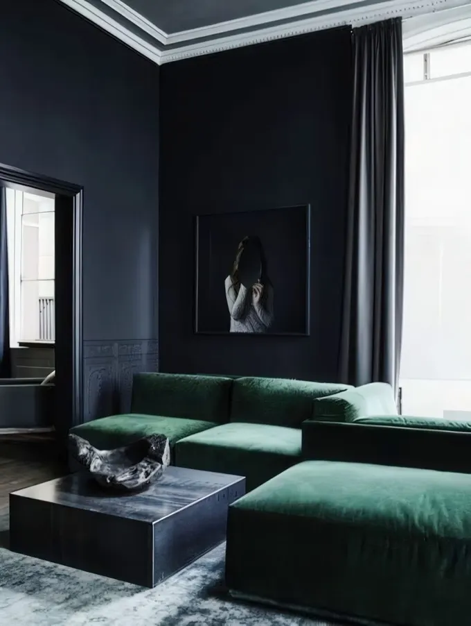 Minimalist oturma odasında siyah duvarlar ve gri tavan, köşedeki yeşil kanepeyle renklere hareket katıyor.
