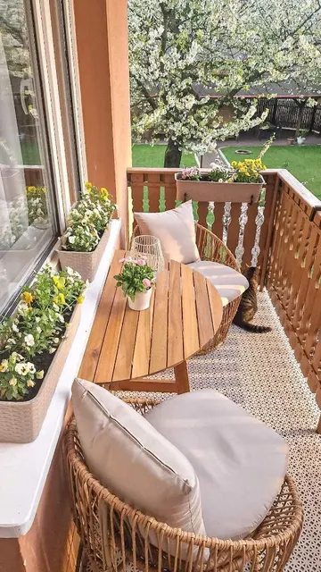 Katlanabilir masa, hasır sandalyeler ve çiçeklerle donatılmış bu balkon çok şirin görünüyor.