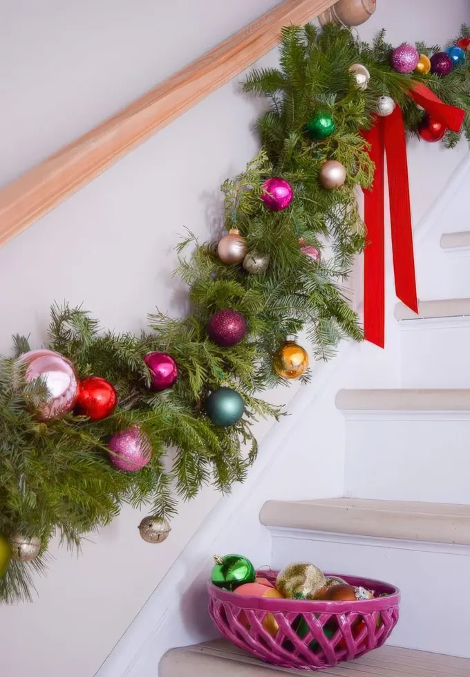 Kırmızı fiyonklarla süslenmiş canlı yeşil ve renkli Noel süslerinden oluşan dekoratif bir süsleme fikri.