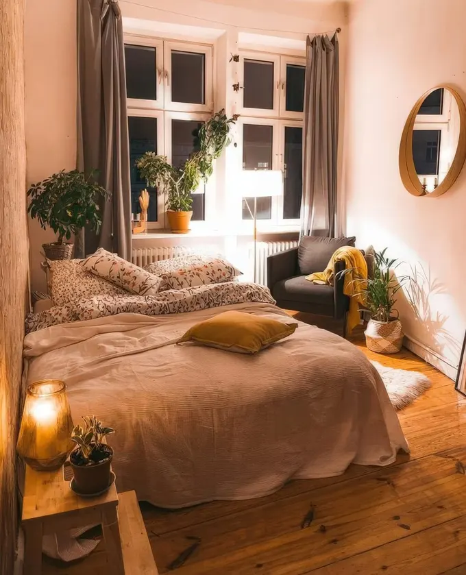 Büyük yatak, saksı bitkileri, yumuşak renkli tekstiller ve duvarda ayna ile küçük boho yatak odası.
