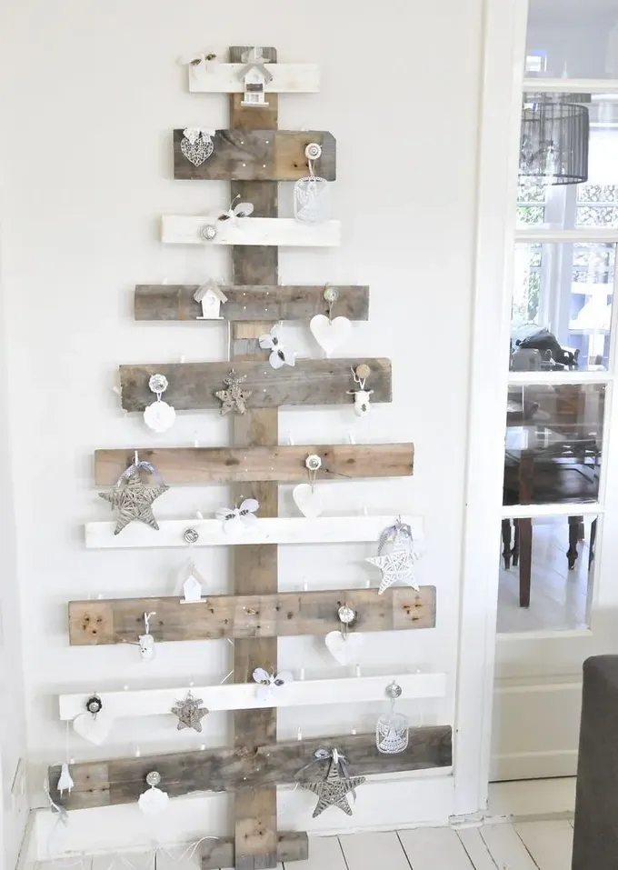 Bu palet ahşap rustik Noel ağacı duvara monte edilmiş ve karışık süslerle dekore edilmiş, yer tasarrufu için ideal bir fikir.