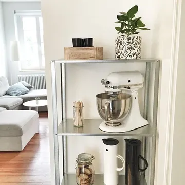 Aydınlık koridorda metal IKEA Hyllis rafı, mikser, kavanozlar ve saksı bitkisiyle temiz ve işlevsel bir görünüm sağlıyor.