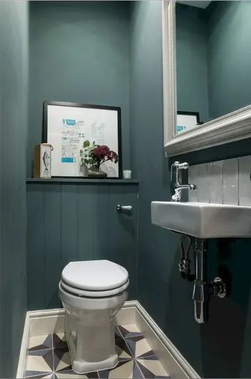 Turkuaz duvarlar, çerçeveli büyük ayna, birkaç sanat eseri ve duvara monteli lavabo bulunan misafir tuvaleti.