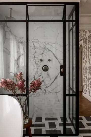 Beyaz mermer ve siyah-beyaz karolar, siyah çerçeveli cam kapılar ve oval küvetli ışıltılı siyah-beyaz banyo.