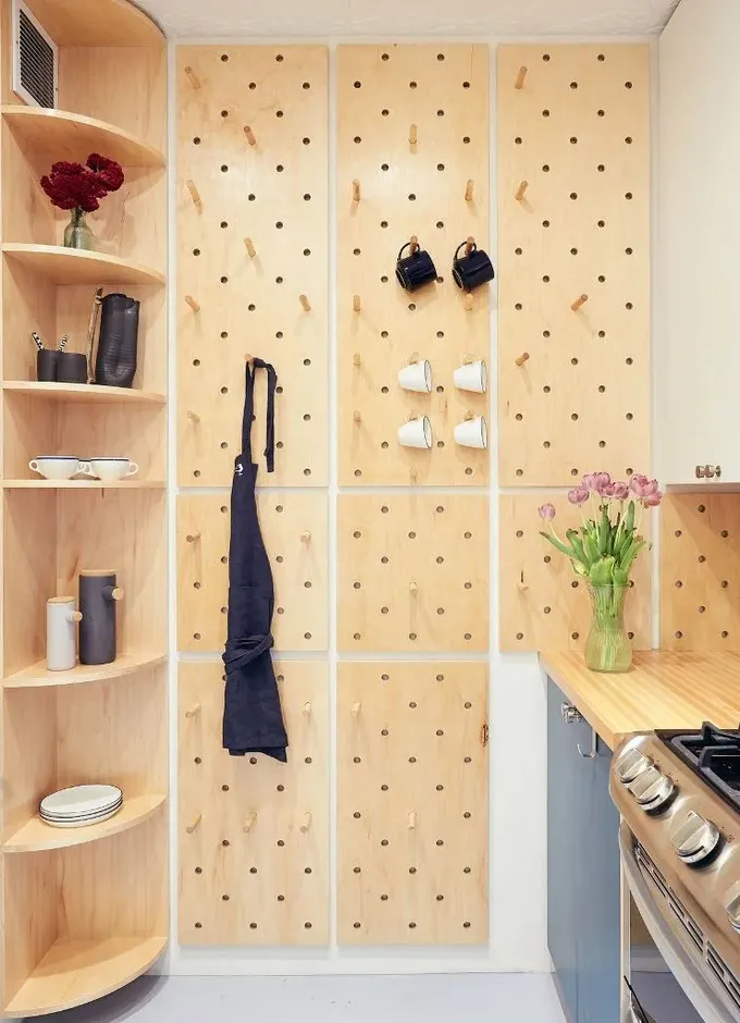 Bir duvar pegboard panelleriyle kaplanmış, kıyafetlerden kupalara kadar her şeyi asıyor.