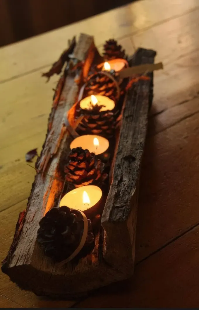 Çam kozalakları ve tealight mumlarla süslenmiş ağaç kütüğü, sonbaharı yansıtan rustik ve havalı bir masa ortasıdır.