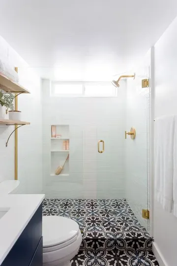 Beyaz duş karoları, desenli zemin, lacivert bir lavabo ve altın dokunuşlarıyla küçük modern banyo.